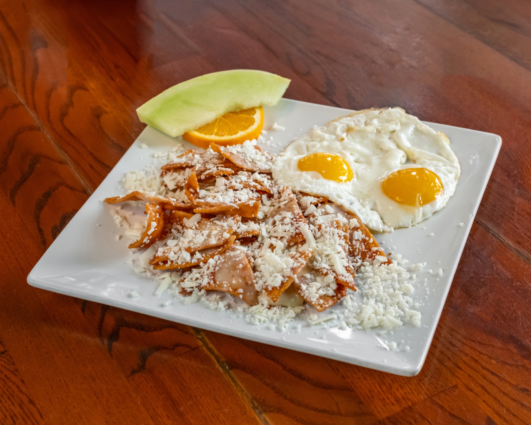 Chilaquiles topped with cheese and served with two sunny-side eggs and fresh fruit